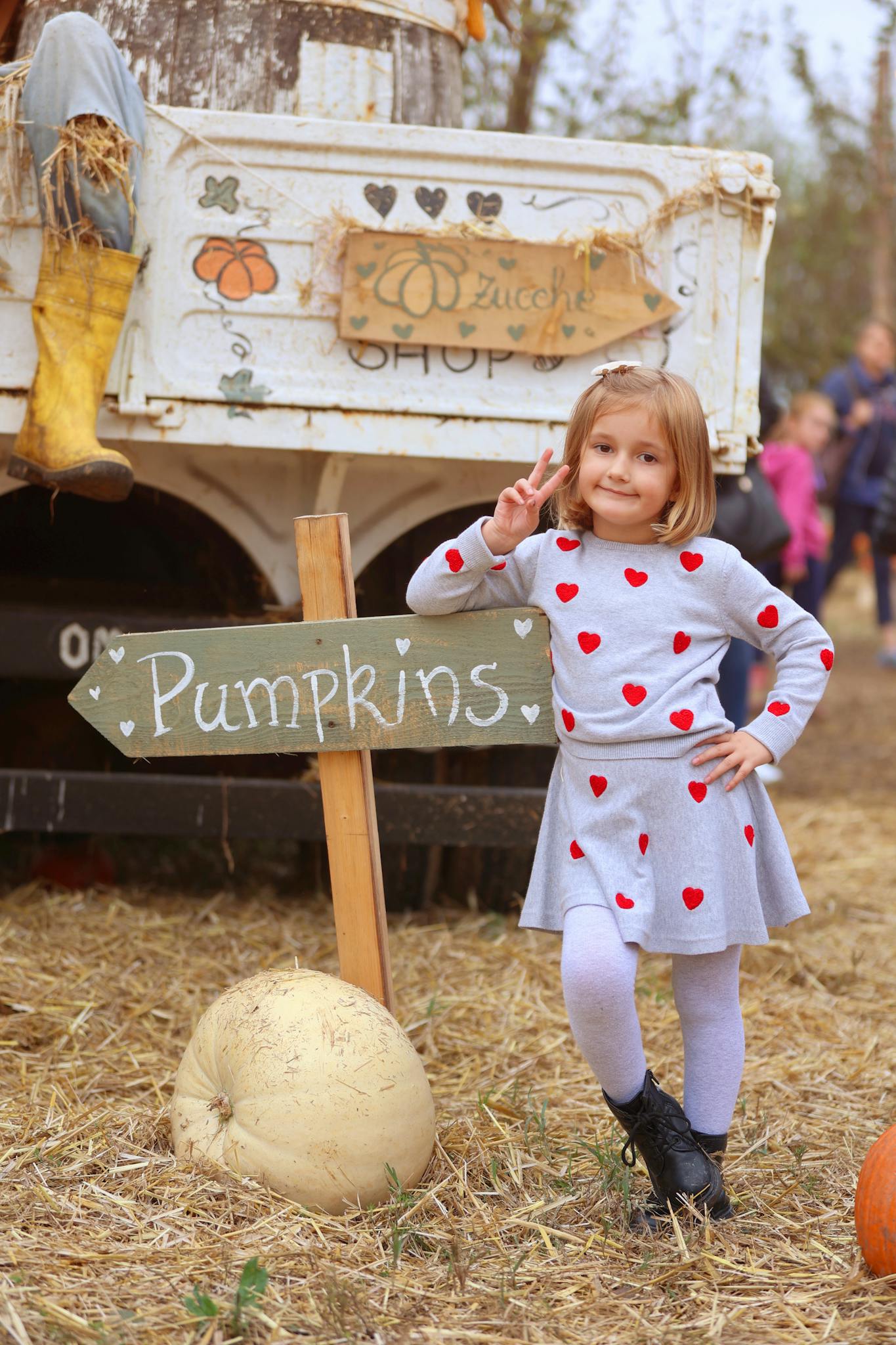 A young girl stands by a pumpkin patch sign, enjoying the autumn atmosphere.