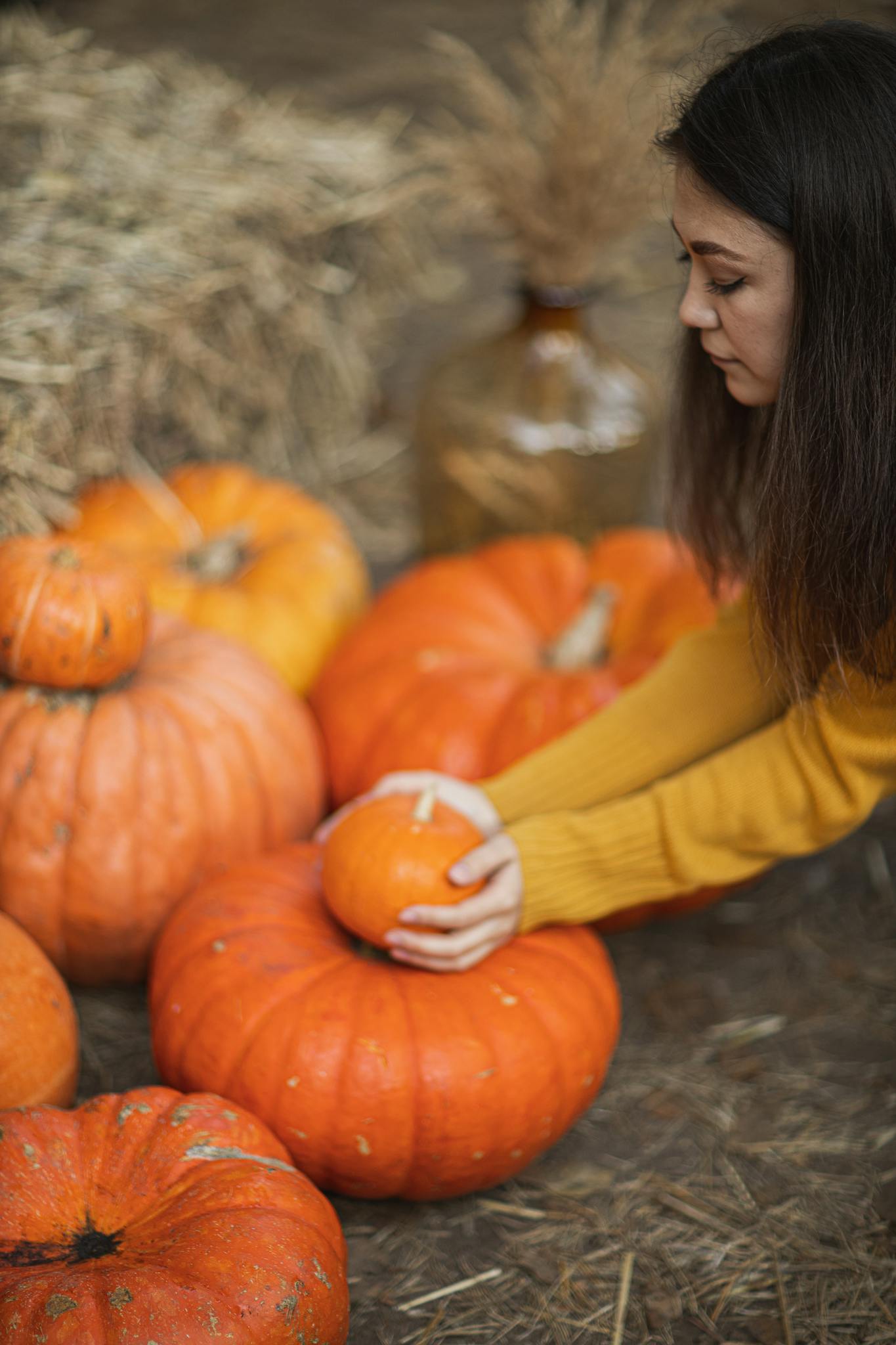 Young woman choosing pumpkins among hay bales during fall harvest.